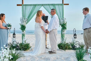 a man and woman holding hands under a wedding arch on a beach